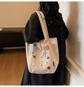 Detail of canvas tote bag showing cat embroidery and plush bear charm on strap