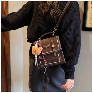 Detail of vintage brown leather handbag with white stitching and bear charm on model
