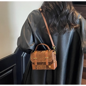 Sac à main marron à texture plissée et fermoir doré porté sur un manteau noir