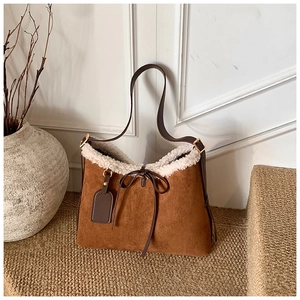 Detail of suede tote with faux shearling trim and decorative bow on woven mat