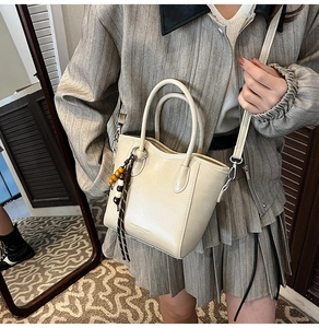 Vue détaillée du sac seau en cuir beige avec pompon perlé et poignées rondes