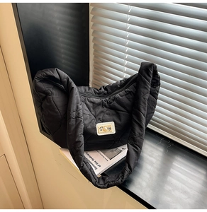 Detail of black quilted shoulder bag featuring heart stitching and pearl logo accent
