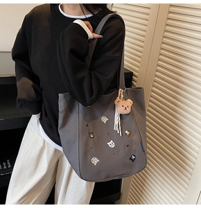 Close-up of animal embroidery and teddy bear charm on grey canvas tote bag