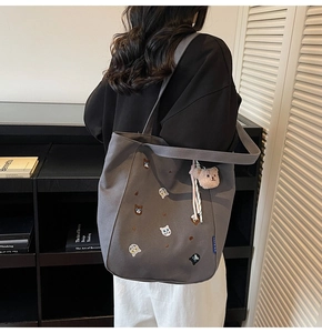 Gray canvas tote bag featuring cat embroidery and a teddy bear charm on model shoulder
