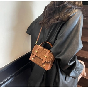 Détail d'un sac bandoulière vintage marron texturé porté sur un manteau en cuir noir