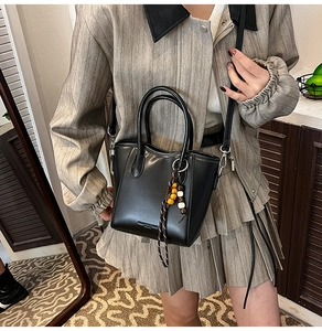 Détail du sac seau minimaliste noir en cuir lisse avec un pendentif décoratif en perles