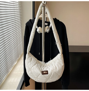 Detail of white quilted crescent bag featuring heart pattern stitching and brand leather patch