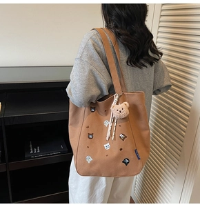 Detail of caramel canvas tote with animal embroidery and plush bear charm shown on model