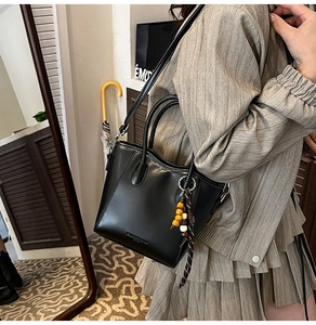 Détail d'un sac seau noir bandoulière avec breloque perlée sur un tailleur rayé