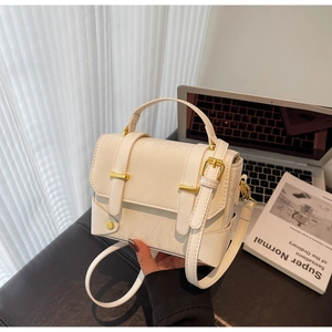 Détail d'un sac bandoulière blanc avec boucles dorées et poignée sur surface en cuir