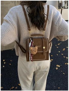Outdoor view of a vintage caramel mini backpack with a teddy bear and ribbon charm