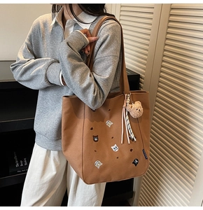 Detail shot of brown canvas tote bag featuring cat embroidery and plush bear charm