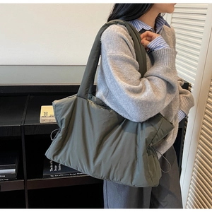 Detailed side view of a grey quilted puffy tote bag with wide shoulder strap design