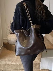 Deep brown leather bucket tote bag with gold chain strap shown on model's shoulder