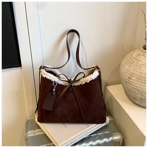 Close-up of brown suede shoulder bag with white faux fur trim and bow detail on books