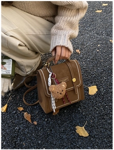 Detail of vintage brown leather handbag with teddy bear charm on autumn leaf ground