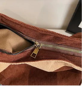 Detail of smooth bronze metal zipper on a two-tone corduroy patchwork shoulder bag