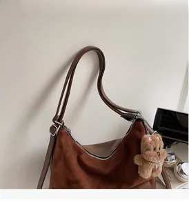 Detail of vintage brown suede tote bag featuring a cute plush bear charm and sturdy strap