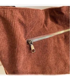 Close-up of brown corduroy fabric texture and smooth golden metal zipper on tote bag