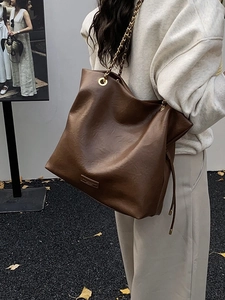 Deep brown bucket tote bag with gold chain strap shown in an outdoor casual setting