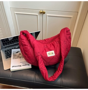 Detail of red crescent shoulder bag with heart quilting and white logo on black surface