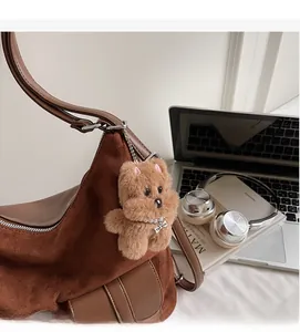 Detail of plush brown dog bag charm with pearl necklace on a suede tote bag