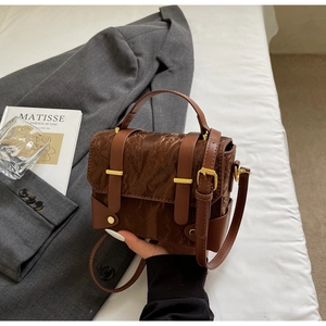 Détail d'un sac bandoulière marron avec texture plissée et boucles dorées sur un lit
