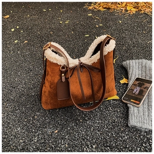 Detail of brown suede tote with white faux shearling trim and decorative bow charm