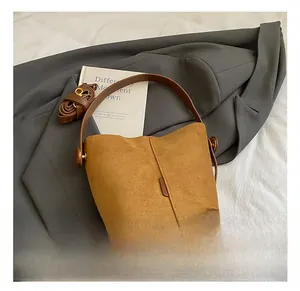 Brown matte suede bucket bag with top handle and adjustable strap on a grey blazer