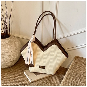 Detail of herringbone straw tote bag with brown leather trim and decorative silk ribbon scarf