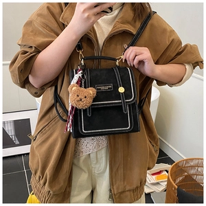 Detail of black mini backpack with contrast stitching and teddy bear charm on model