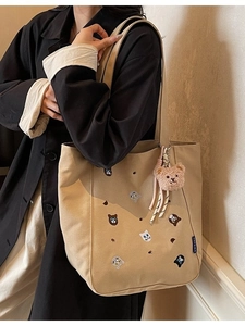 Large beige canvas tote bag with cat embroidery and pink plush charm shown on model shoulder