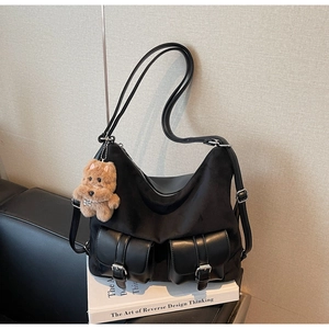 Detail view of black commuter tote bag with leather buckle pockets and teddy bear charm