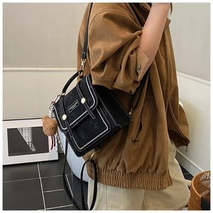 Detail of vintage black backpack with white contrast stitching and bear charm