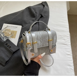 Détail d'un sac argenté à texture marbrée avec boucles dorées et finitions métalliques