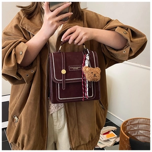 Detail of burgundy leather handbag with stitching, plush bear charm, and plaid scarf
