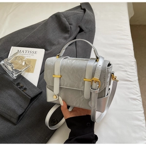 Détail du sac bandoulière argenté à texture marbrée et boucles dorées sur fond gris