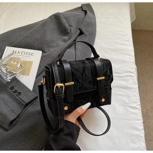 Gros plan du sac bandoulière en velours noir avec fermoir doré sur un fond minimaliste chic