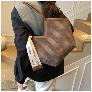 Brown herringbone tote bag featuring asymmetrical cut and leather handles in a lifestyle setting