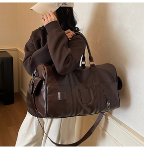 Détail du sac de voyage en cuir marron foncé avec poignées renforcées et bandoulière réglable