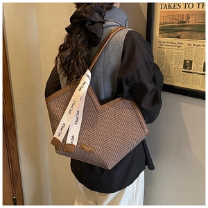 Detail of herringbone tote bag with dark brown leather trim and side decorative ribbon