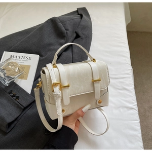 Détail du sac à main en cuir blanc avec boucle dorée, poignée et bandoulière réglable