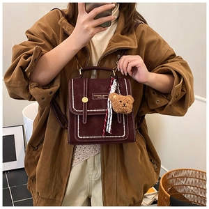 Mirror selfie showing a vintage dark red mini backpack with plush bear charm and stitch detail