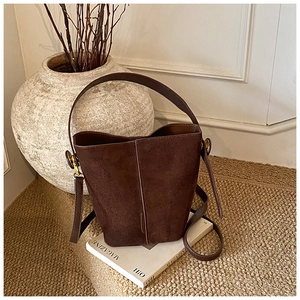 Detail of a dark brown suede bucket bag with gold hardware and a vintage minimalist design