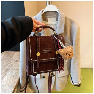 Close-up of vintage burgundy backpack with white stitching and plush bear charm