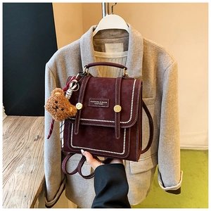 Detailed macro view of the burgundy retro faux leather backpack with metal buckle and plush bear