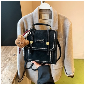 Detail of black matte mini backpack with white stitching and a cute brown bear charm