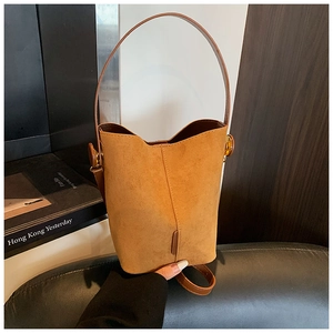 Close-up of brown suede bucket bag with hand-held strap and fine stitching detail
