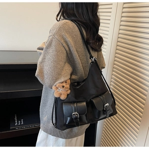Detail view of black nylon tote bag featuring front flap pockets and a plush bear pendant