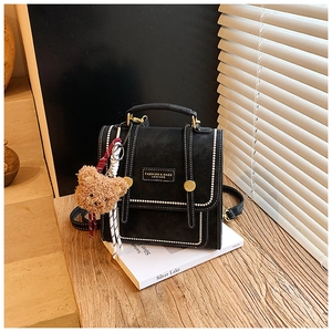 Detail of vintage black leather backpack with white stitching and cute bear charm
